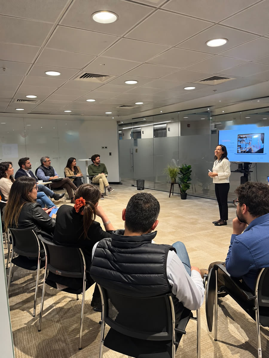 Myriam Jiménez facilitando una sesión frente a un grupo de profesionales sentados en semicírculo, junto a una pantalla